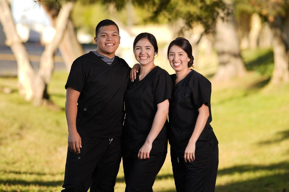 Group of {{ school.name }} students posing together in scrubs outside of school facility Group of {{ school.name }} students posing together in scrubs outside of school facility
